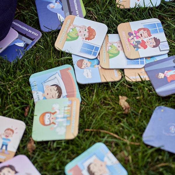 Zdjęcie prezentuje karty do gry "Memory o emocjach" rozłożone na trawie.