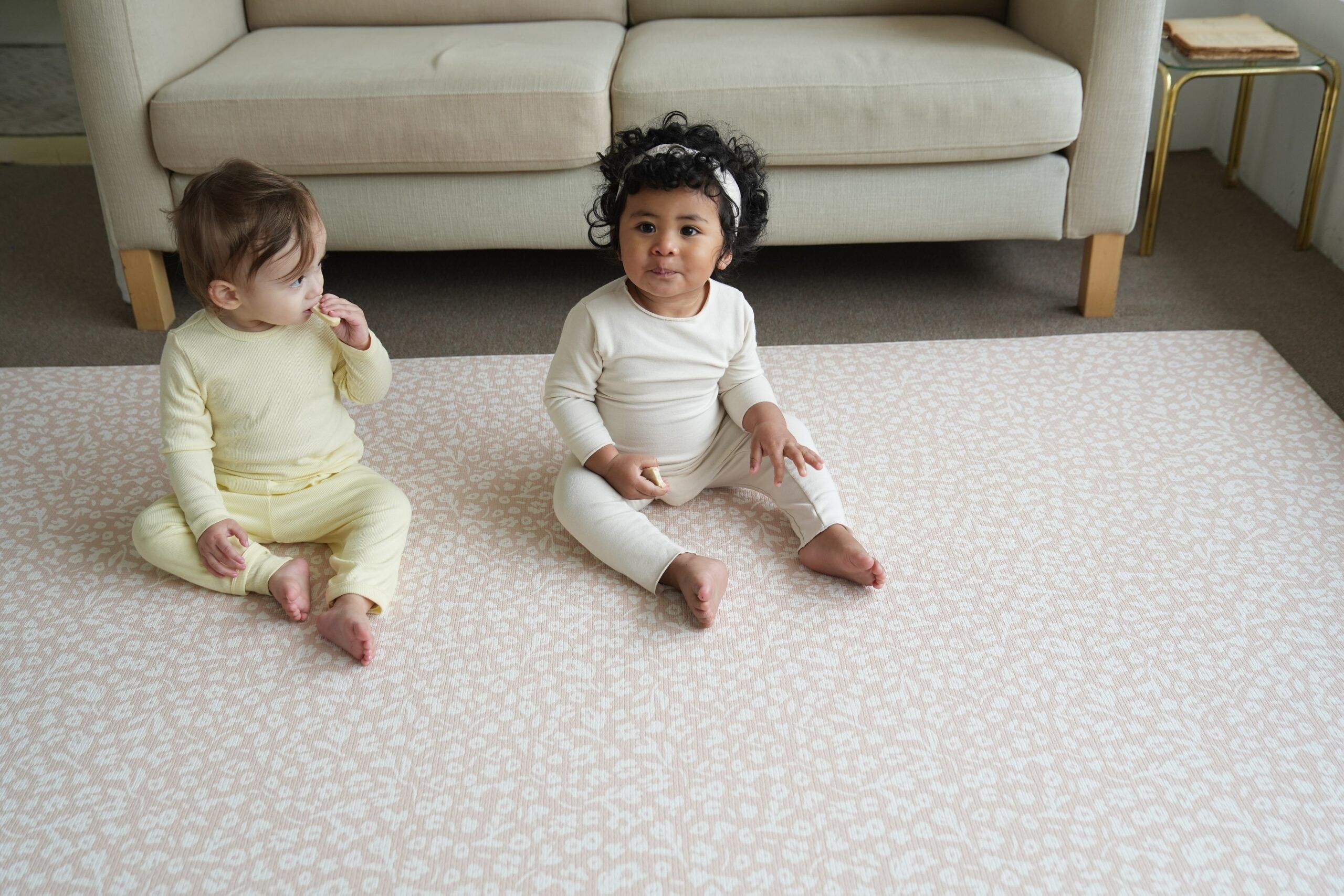 Dziecko siedzące na dwustronnej macie do zabawy marki Dwinguler w jasnym wnętrzu. Mata posiada delikatny wzór, zapewniając bezpieczną i komfortową przestrzeń do raczkowania i zabawy.