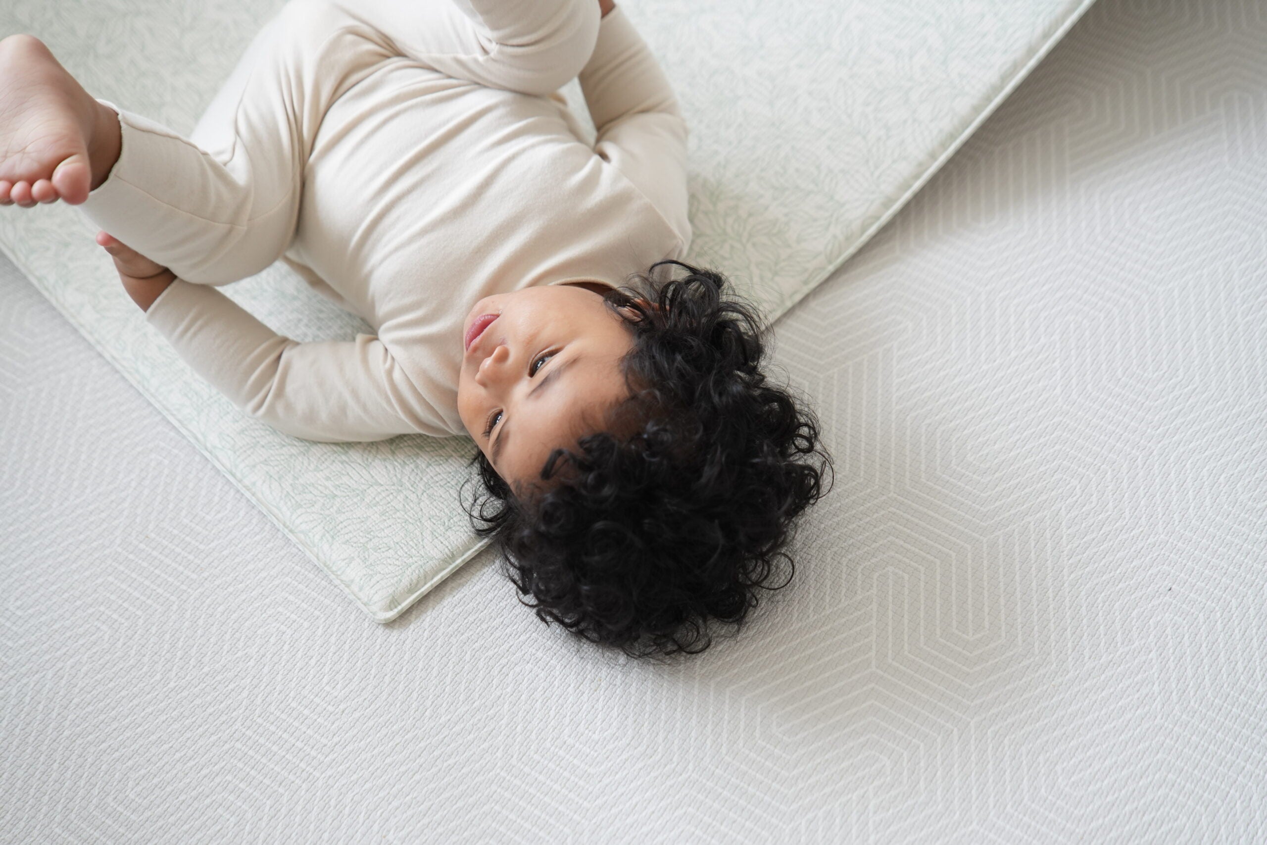 Dziecko siedzące na dwustronnej macie do zabawy marki Dwinguler w jasnym wnętrzu. Mata posiada delikatny wzór, zapewniając bezpieczną i komfortową przestrzeń do raczkowania i zabawy.