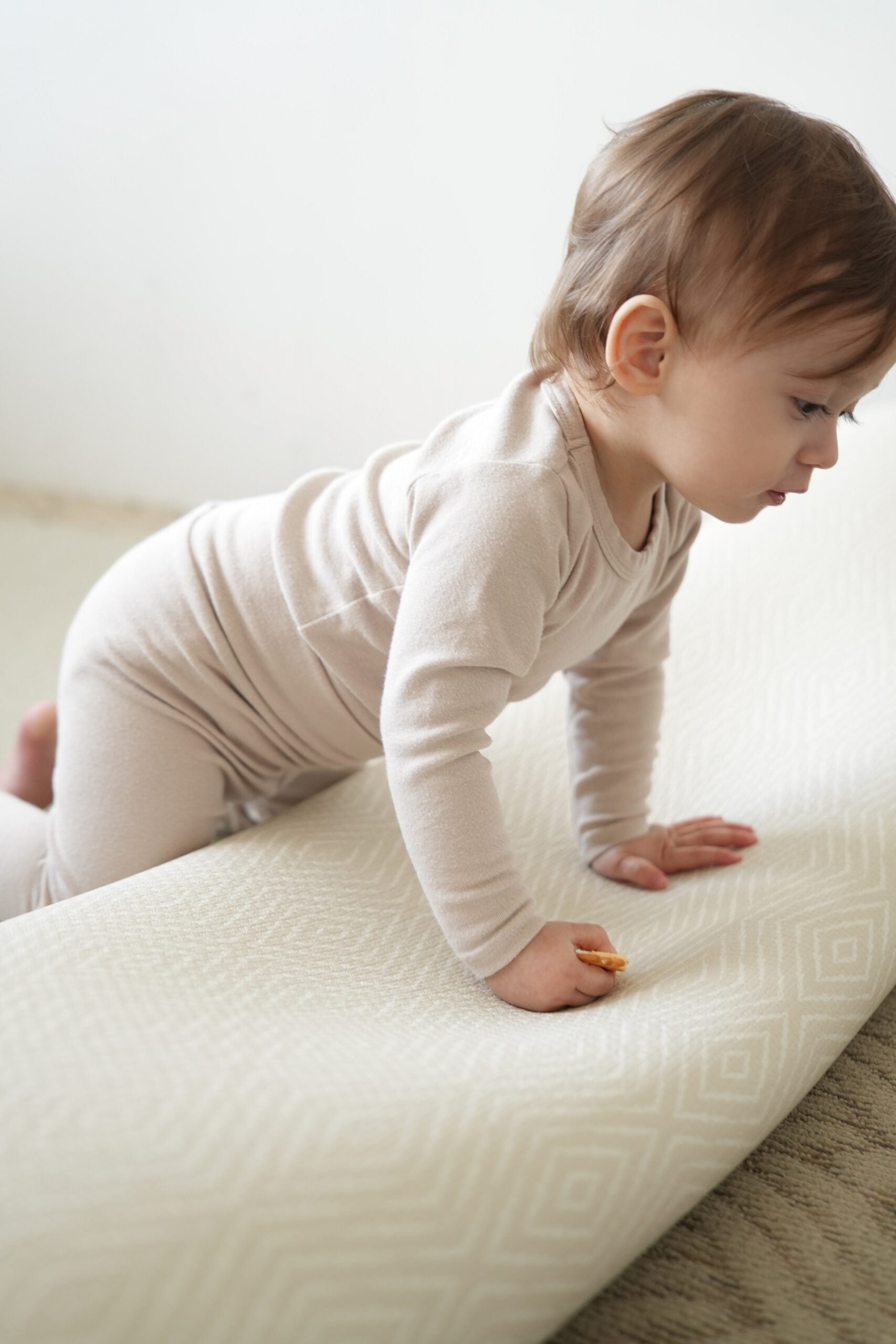 Dziecko siedzące na dwustronnej macie do zabawy marki Dwinguler w jasnym wnętrzu. Mata posiada delikatny wzór, zapewniając bezpieczną i komfortową przestrzeń do raczkowania i zabawy.