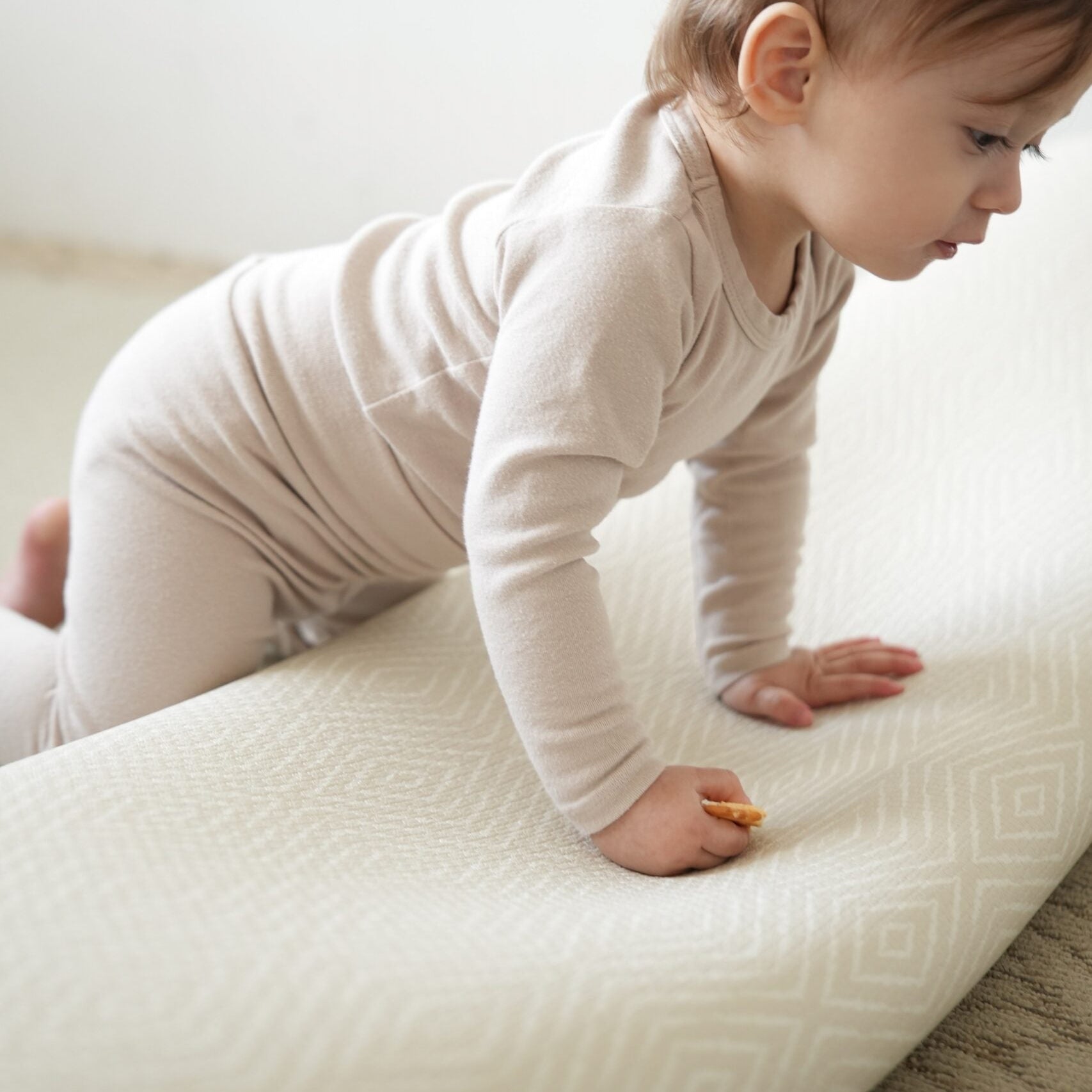 Dziecko siedzące na dwustronnej macie do zabawy marki Dwinguler w jasnym wnętrzu. Mata posiada delikatny wzór, zapewniając bezpieczną i komfortową przestrzeń do raczkowania i zabawy.