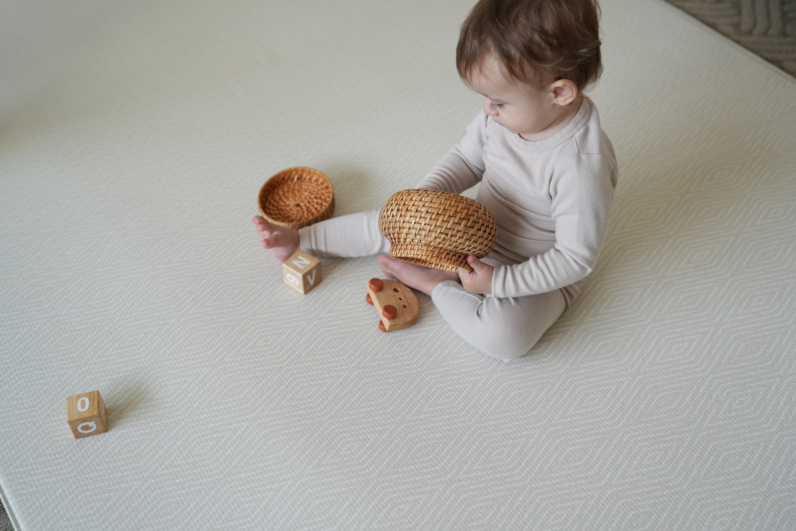Dziecko siedzące na dwustronnej macie do zabawy marki Dwinguler w jasnym wnętrzu. Mata posiada delikatny wzór, zapewniając bezpieczną i komfortową przestrzeń do raczkowania i zabawy.