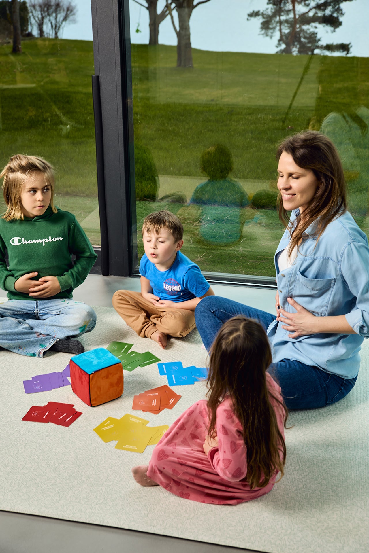 Na zdjęciu kobieta i troje dzieci grających w grę "Kostka aktywności - mindfulness"