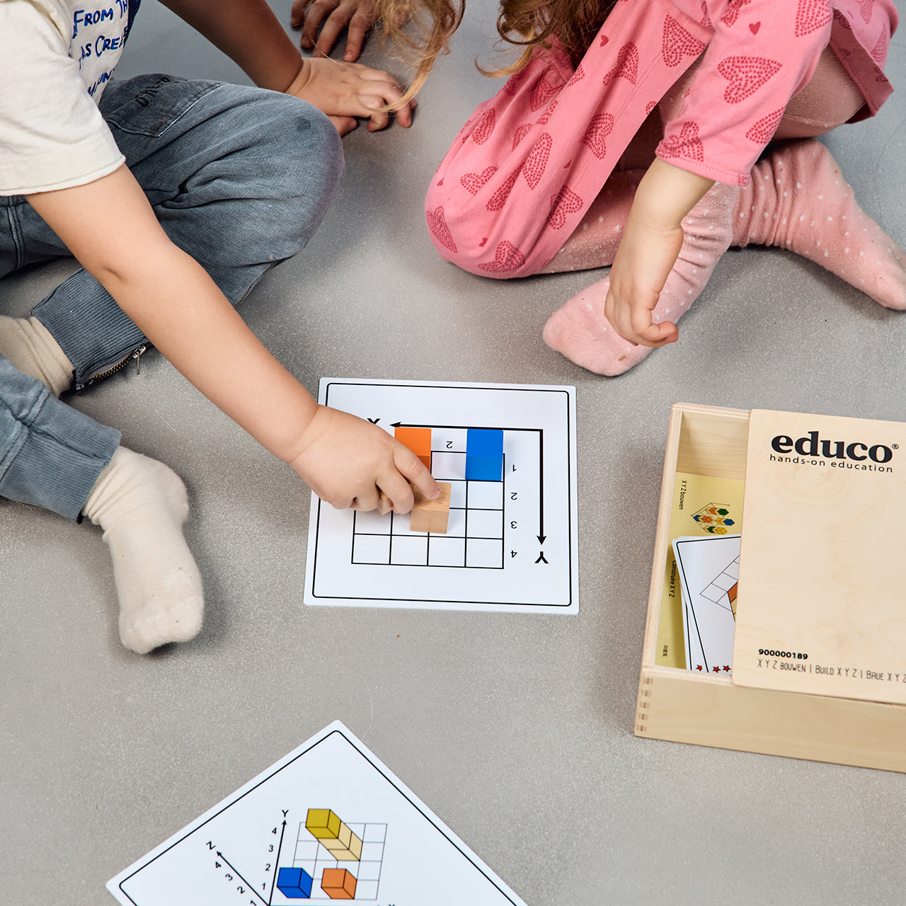 Zestaw Klocki XYZ, który składa się z kolorowych klocków, drewnianych elementów i kart z zadaniami. Gra wspiera rozwój umiejętności matematycznych, inżynieryjnych i językowych u dzieci, ucząc ich budowania konstrukcji w oparciu o wzory 2D i 3D.