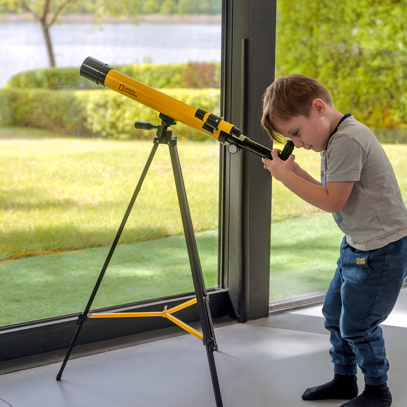 Teleskop Bresser 45/600 mm z rodziny National Geographic, w kolorze żółtym, umieszczony na statywie, przeznaczony do obserwacji astronomicznych, z lunetką celowniczą, różnymi okularami do zmiany powiększenia oraz możliwością użycia do obserwacji przyrody, idealny dla dzieci od 7 roku życia.