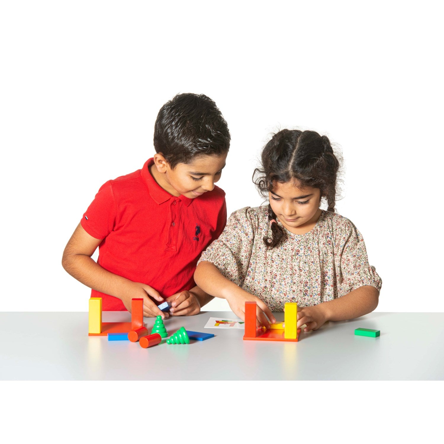 Drewniany zestaw klocków konstrukcyjnych Montessori składający się z kolorowych klocków w różnych kształtach: czerwonej i żółtej płyty, niebieskich prostokątów, zielonych i czerwonych cylindrów oraz dwóch drewnianych figurek w kształcie drzewa i goblina, z kartami z zadaniami do odwzorowania.