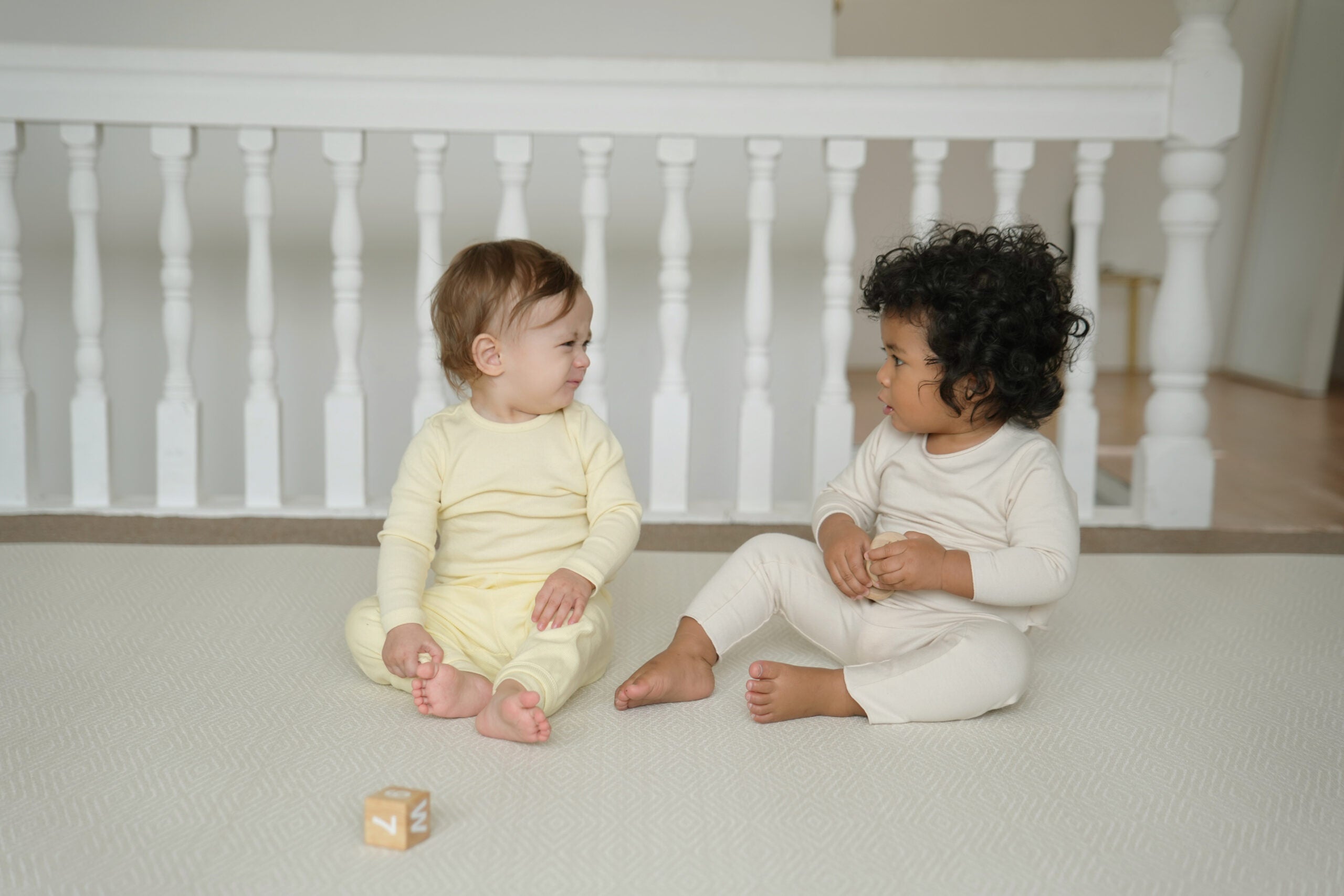 Dziecko siedzące na dwustronnej macie do zabawy marki Dwinguler w jasnym wnętrzu. Mata posiada delikatny wzór, zapewniając bezpieczną i komfortową przestrzeń do raczkowania i zabawy.