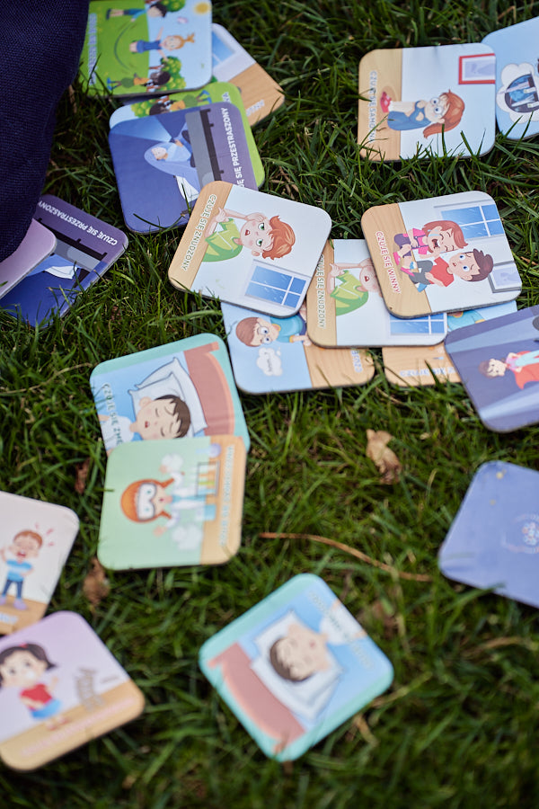 Zdjęcie prezentuje karty do gry "Memory o emocjach" rozłożone na trawie.