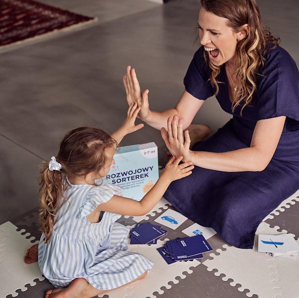 Zdjęcie przedstawia kobietę i dziewczynkę grające w grę "Rozwojowy sorterek".