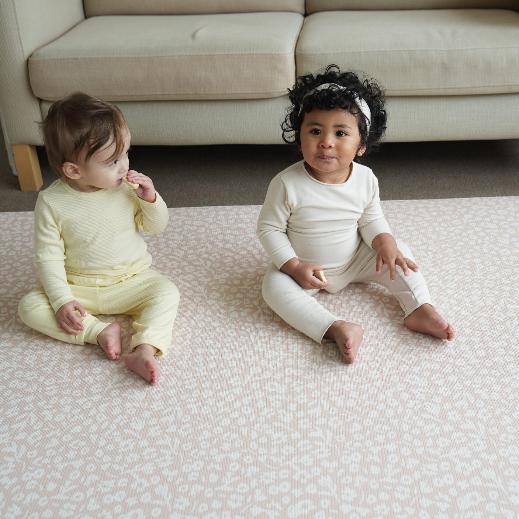 Dziecko siedzące na dwustronnej macie do zabawy marki Dwinguler w jasnym wnętrzu. Mata posiada delikatny wzór, zapewniając bezpieczną i komfortową przestrzeń do raczkowania i zabawy.