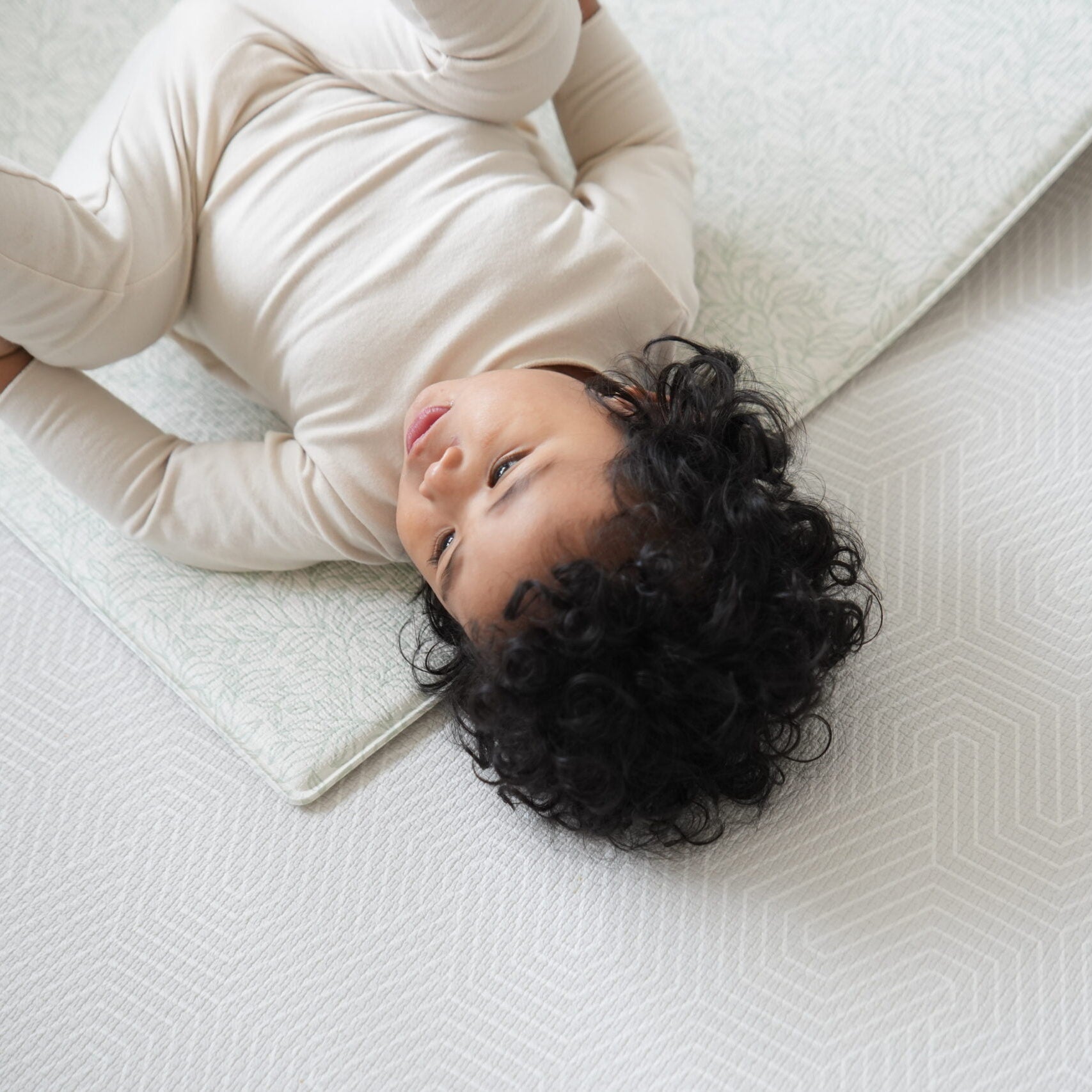 Dziecko siedzące na dwustronnej macie do zabawy marki Dwinguler w jasnym wnętrzu. Mata posiada delikatny wzór, zapewniając bezpieczną i komfortową przestrzeń do raczkowania i zabawy.