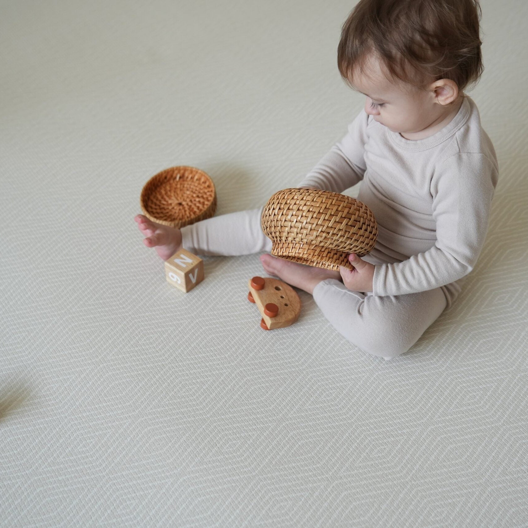 Dziecko siedzące na dwustronnej macie do zabawy marki Dwinguler w jasnym wnętrzu. Mata posiada delikatny wzór, zapewniając bezpieczną i komfortową przestrzeń do raczkowania i zabawy.