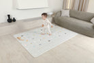 Dziecko stojące na dwustronnej macie do zabawy marki Dwinguler w jasnym wnętrzu. Mata posiada delikatny wzór, zapewniając bezpieczną i komfortową przestrzeń do raczkowania i zabawy.