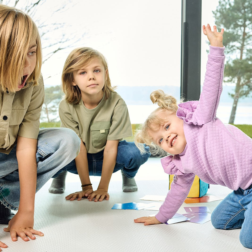 Na zdjęciu troje dzieci grających w grę "Kostka aktywności"