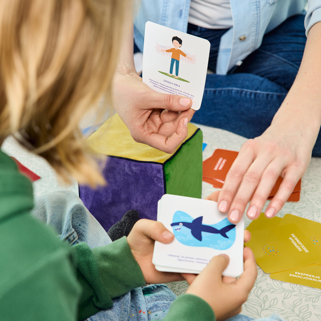 Na zdjęciu widoczne dłonie kobiety i dziecka; trzymają karty z zadaniami do gry "Kostka aktywności - mindfulness"
