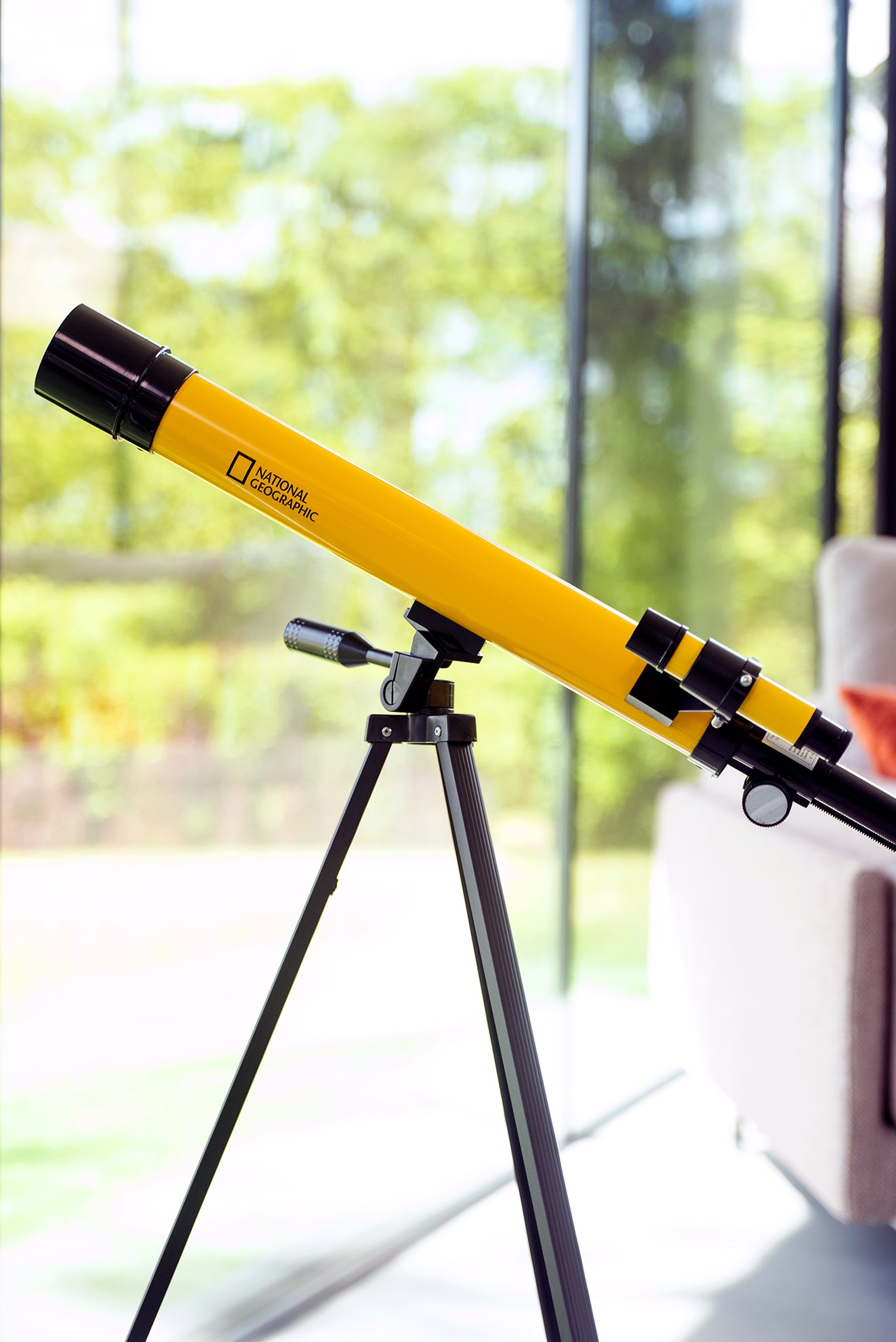 Teleskop Bresser 45/600 mm z rodziny National Geographic, w kolorze żółtym, umieszczony na statywie, przeznaczony do obserwacji astronomicznych, z lunetką celowniczą, różnymi okularami do zmiany powiększenia oraz możliwością użycia do obserwacji przyrody, idealny dla dzieci od 7 roku życia.
