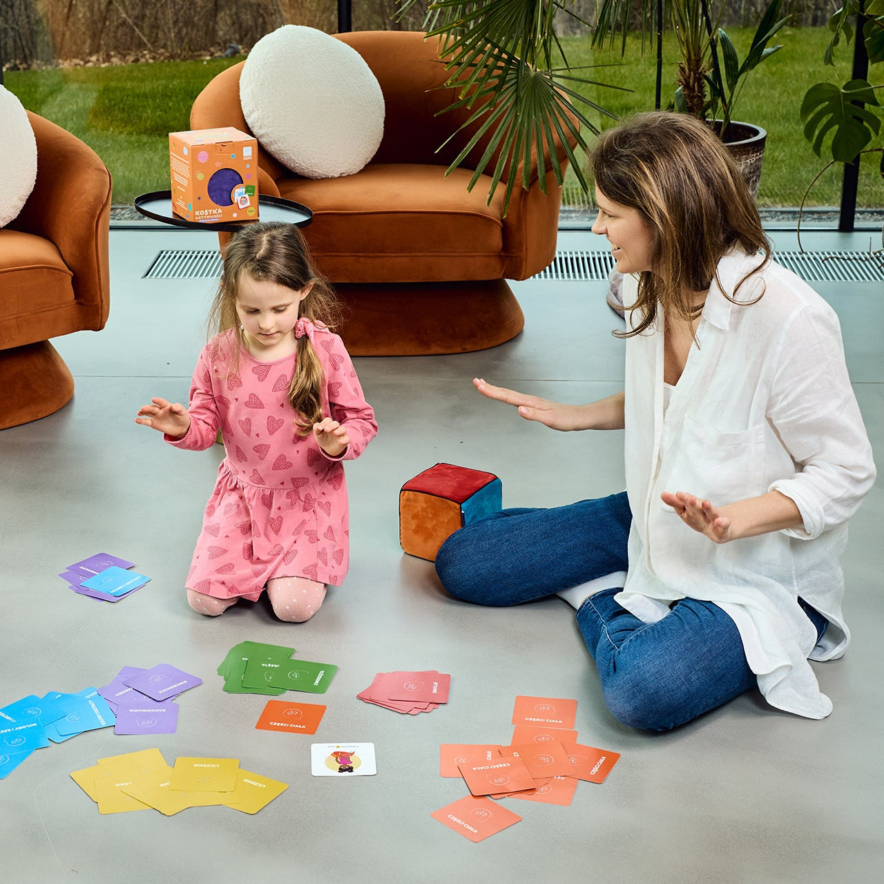 Mama i dwoje dzieci grających na podłodze w Nauka przez Zabawę – chłopiec i dziewczynka wykonują zadania z kart