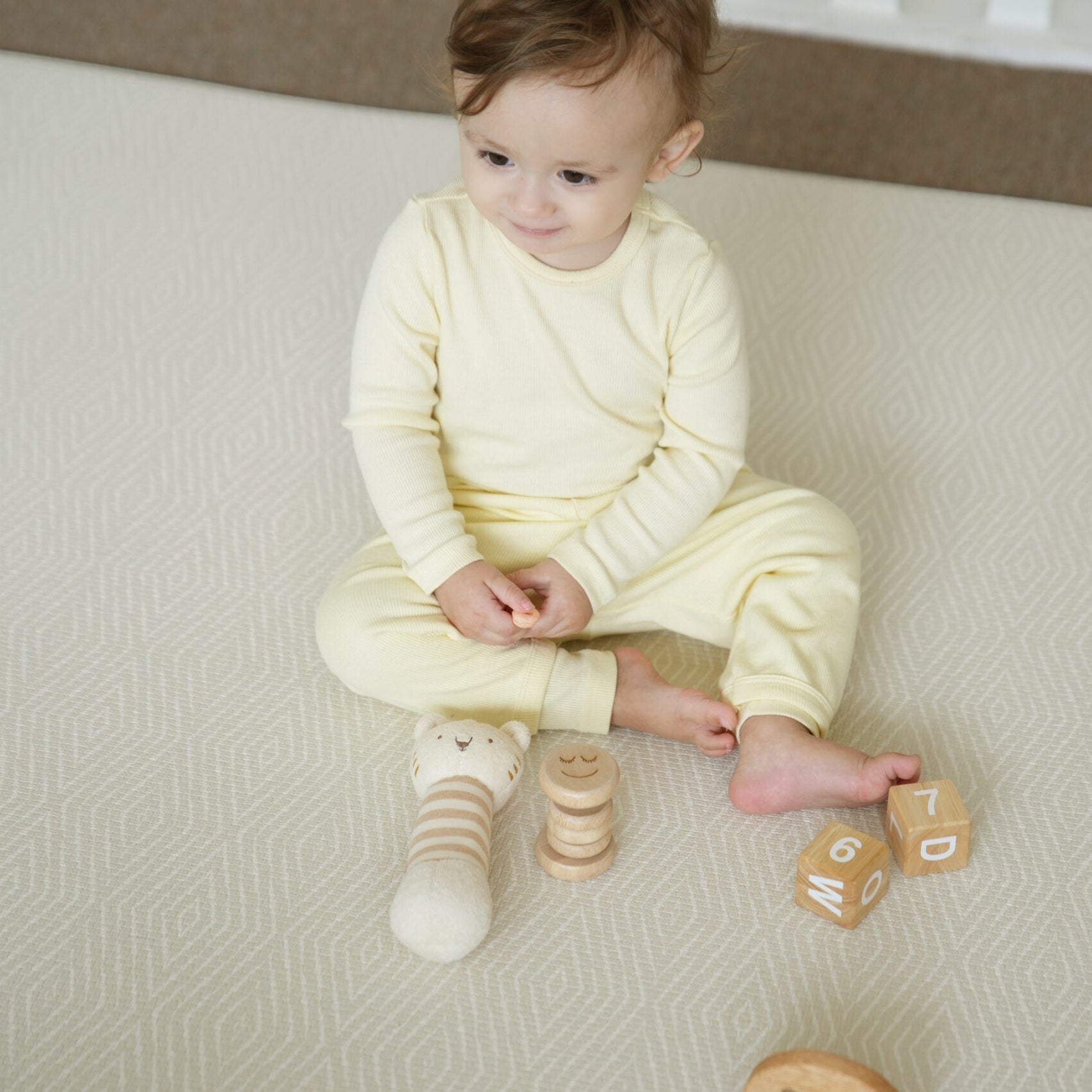 Dziecko siedzące na dwustronnej macie do zabawy marki Dwinguler w jasnym wnętrzu. Mata posiada delikatny wzór, zapewniając bezpieczną i komfortową przestrzeń do raczkowania i zabawy.