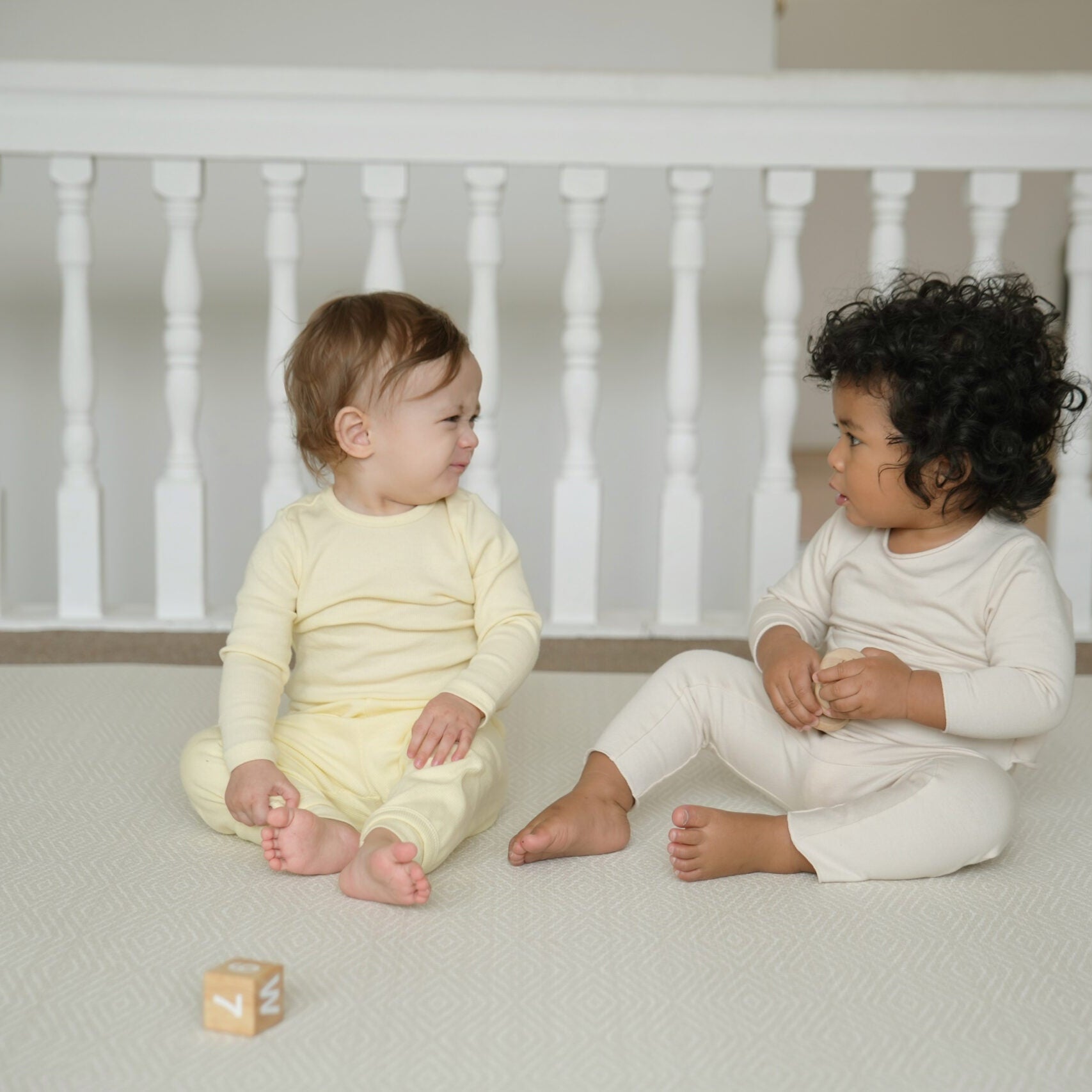 Dziecko siedzące na dwustronnej macie do zabawy marki Dwinguler w jasnym wnętrzu. Mata posiada delikatny wzór, zapewniając bezpieczną i komfortową przestrzeń do raczkowania i zabawy.