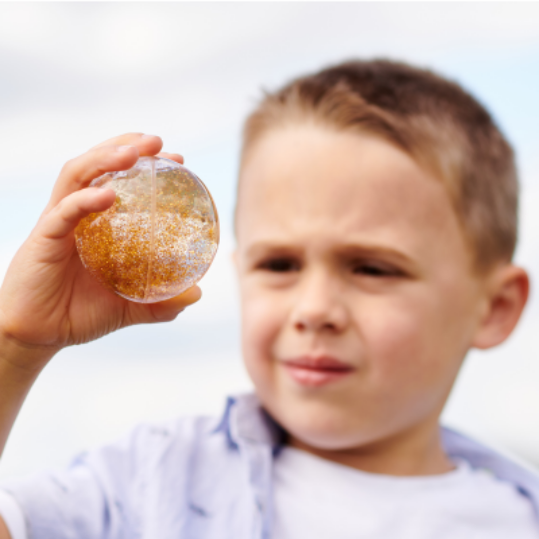 Zbliżenie na brokat w kulach sensorycznych TickiT – tęczowe kolory i unoszący się brokat stymulujący zmysł wzroku dziecka